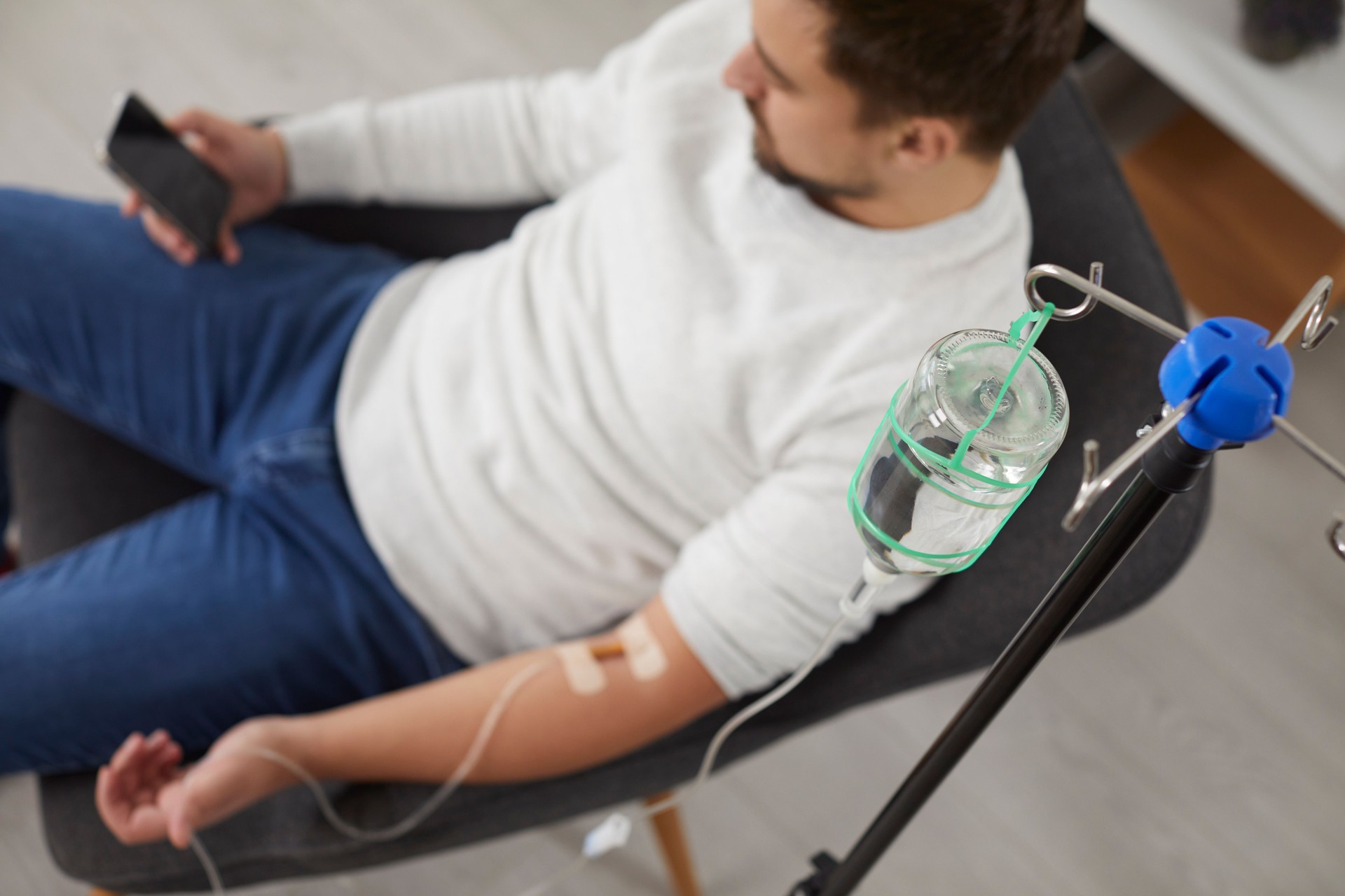 Top view image of a man receiving IV drip infusion and vitamin therapy sitting in chair.
